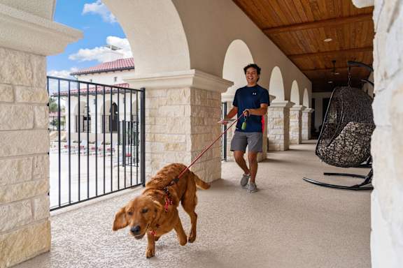A man walking his dog on a leash in a covered walkway.