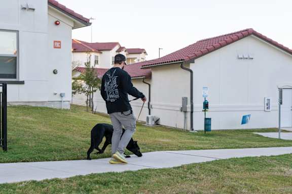 A man walking a dog on a leash in front of a white building.