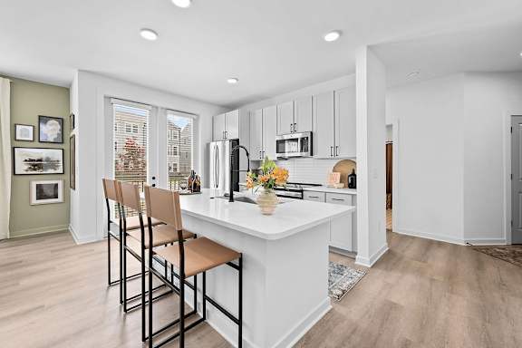 A kitchen with a white island and brown barstools.