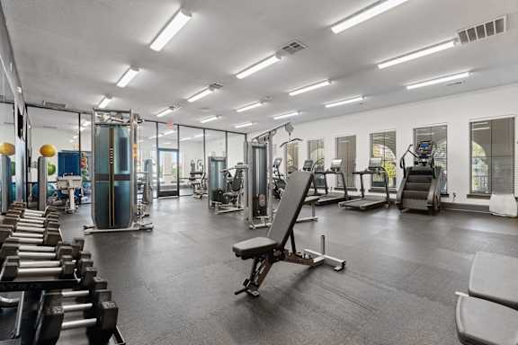 A gym with a variety of equipment including dumbbells, weight machines, and a bench press.