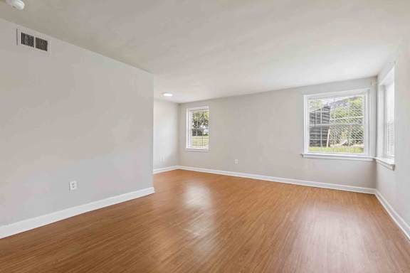 A room with wooden flooring and two windows.