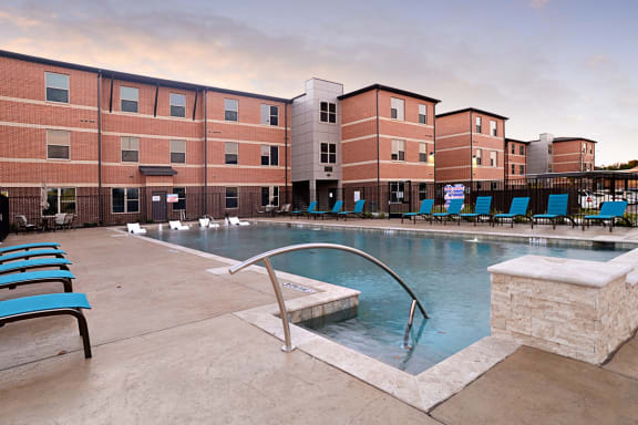 an image of a city with a pool and buildings with orange lights at The Liberty Lofts, Gainesville, 76240