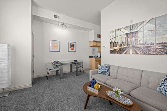 A living room with a grey couch, a coffee table, and a painting of a bridge on the wall.