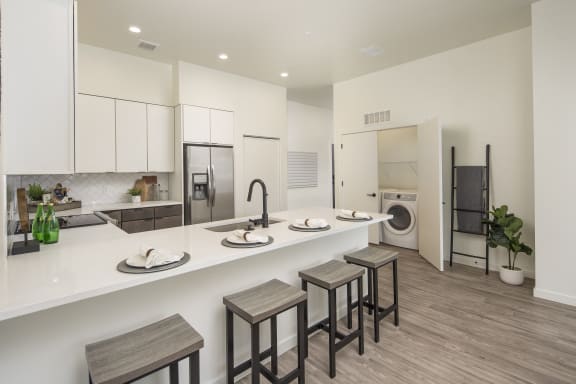 a white kitchen with a long counter top and some bar stools