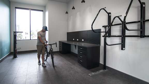 a man is holding a bike in a room with a desk and a bike rack at Cycle Apartments, Colorado, 80525
