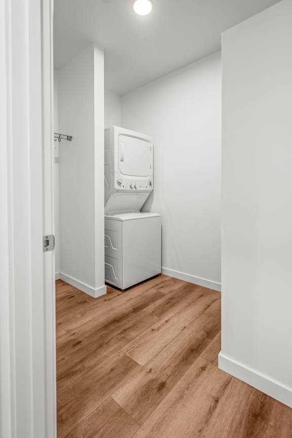 A white washing machine is in a small room with wooden floors.
