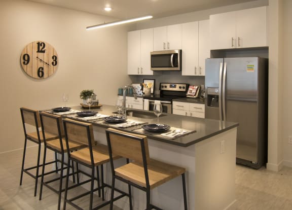 a kitchen with a large island with bar stools and a stainless steel refrigerator at Cycle Apartments, Fort Collins
