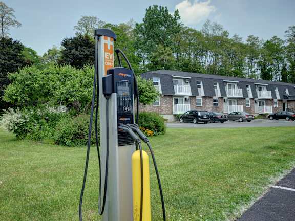 An electric vehicle charging station is located in a grassy area near apartment buildings.