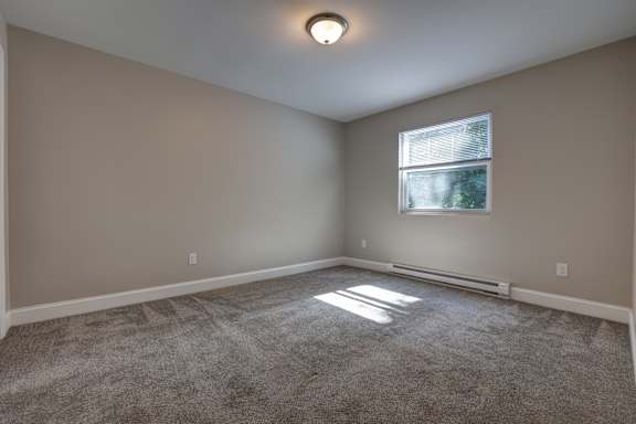 A room with a window and a carpeted floor.