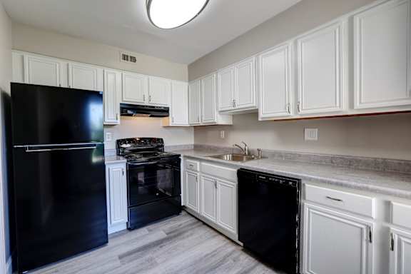 A black refrigerator is in a kitchen with white cabinets.