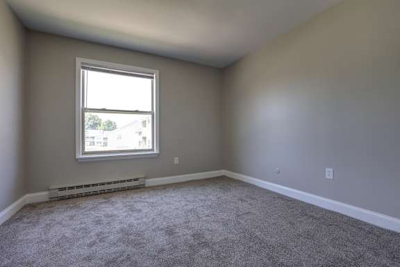 A room with a window and a carpeted floor.