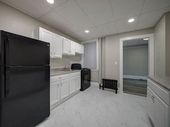 A black refrigerator is in a kitchen with white cabinets at Willett Apartments, Albany, New York