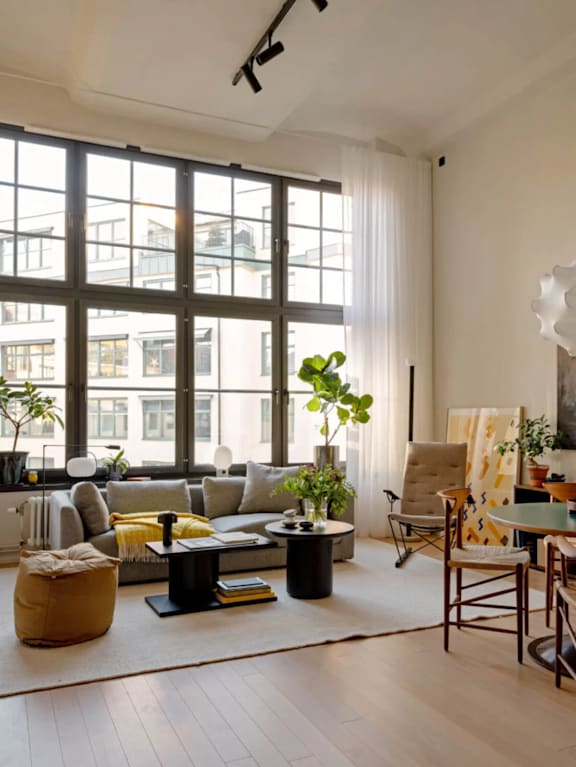 A living room with a large window, a sofa, a chair, a table, and a potted plant.