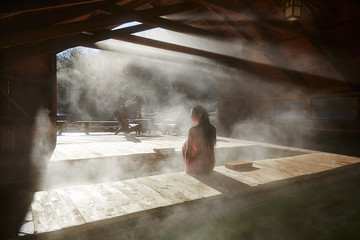 A person is sitting on a wooden platform in a misty, dimly lit room.