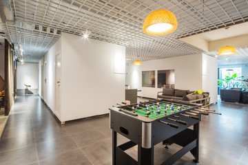 A foosball table is in the middle of a room with a white ceiling and a long hallway.