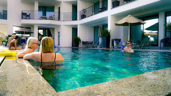 A woman in a black bikini is sitting by a pool.