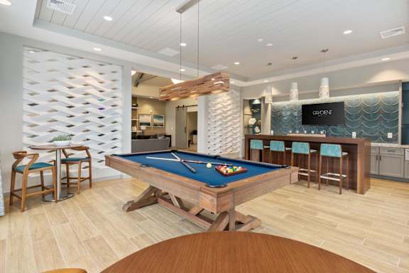 A pool table is in the middle of a room with a bar and a TV.