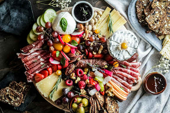 A variety of cheeses, meats, and fruits are arranged on a platter.