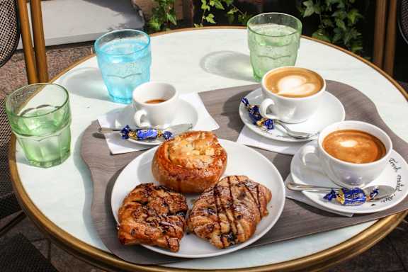 A table with a plate of food and two cups of coffee.
