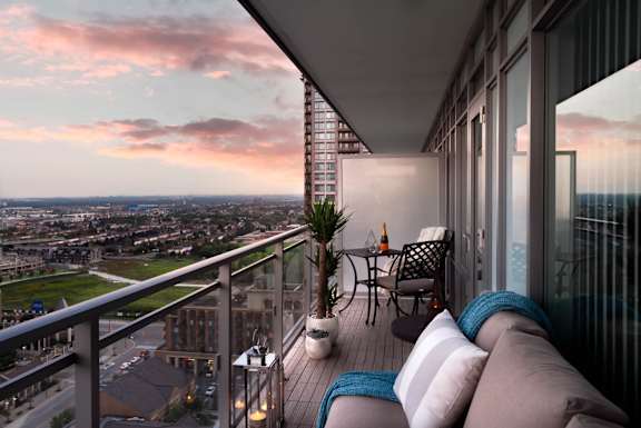 A balcony with a table and chairs overlooking a cityscape at sunset.