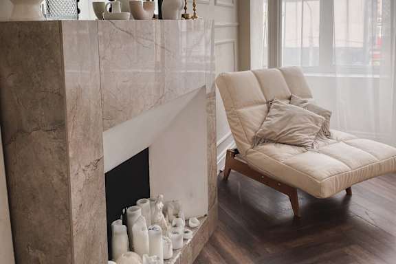 A white chair with a cushion is placed in front of a marble fireplace.