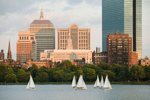 Three sailboats are sailing on a body of water in front of a city skyline.