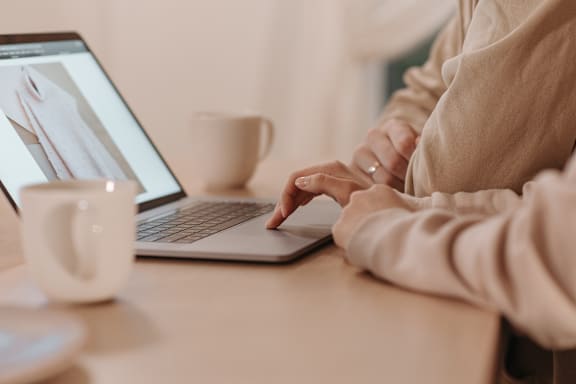 A person is typing on a laptop with a cup of coffee on the table.