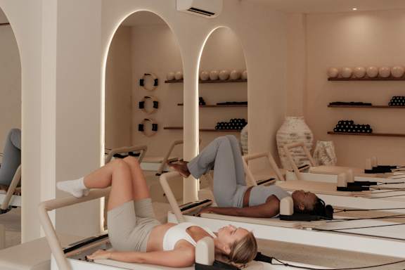 Two women are lying on reformers in a pilates studio.