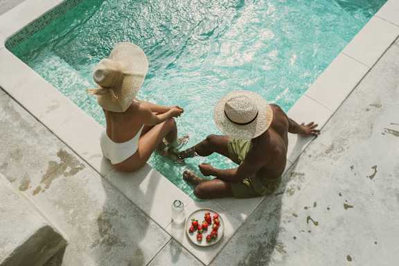 Two people sitting by a pool with a plate of food in front of them.