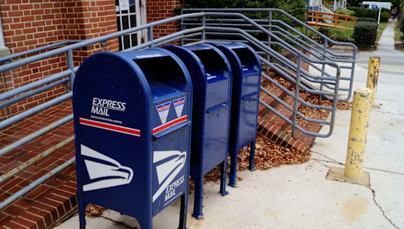 A row of blue mailboxes are lined up on a sidewalk.