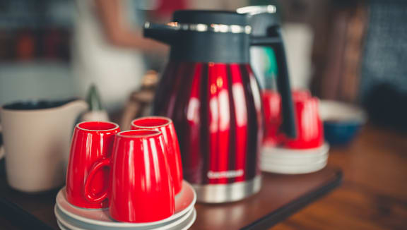 A red coffee pot and cups are on a table.