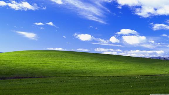 A field of green grass under a blue sky with clouds.