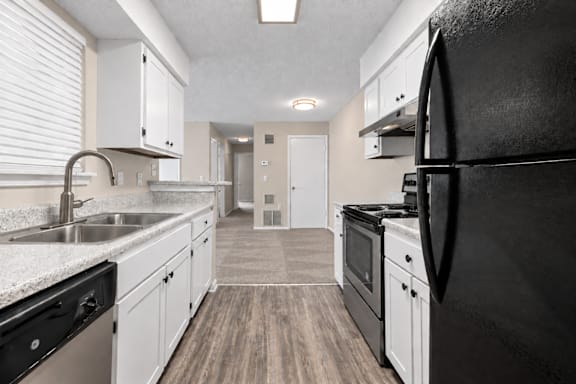 A black refrigerator is in the corner of a kitchen with white cabinets.