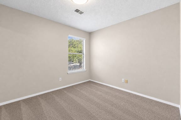 A room with a carpeted floor and a window with blinds.