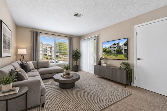 A living room with a grey couch, a coffee table, and a flat screen TV mounted on the wall.