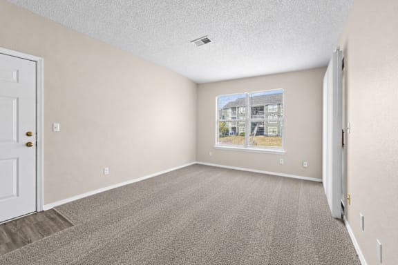 A room with a carpeted floor and a window showing an apartment building outside.