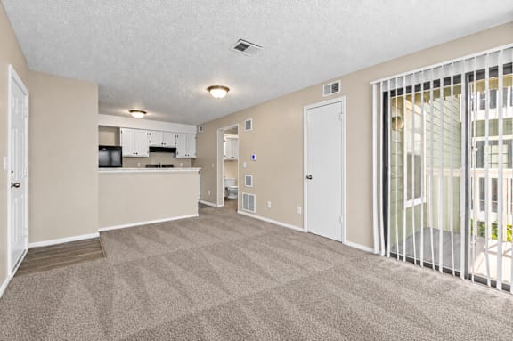 A spacious room with a carpeted floor and a kitchen area in the background.