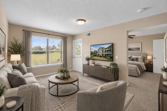 A living room with a grey couch, a coffee table, and a large window with a view of the outside.