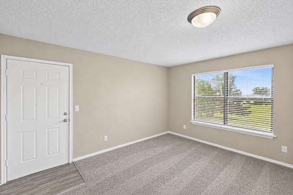 A room with a white door, carpeted floor, and a window with blinds.