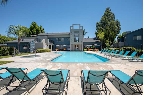 A pool surrounded by lawn chairs in front of a building at Autumn Oaks Apartments, Roseville, CA, 95678