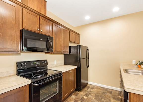 A kitchen with black appliances and wooden cabinets at The Landing Apartments and Townhomes, Oregon, 97045