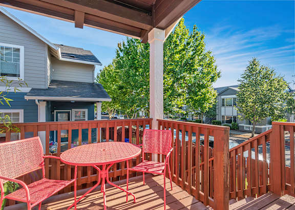 A red table and chairs are on a wooden deck at The Landing Apartments and Townhomes, Oregon, 97045