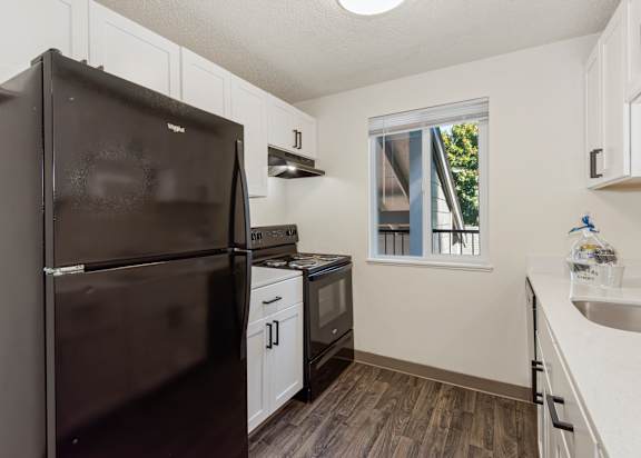 A black refrigerator is in a kitchen with white cabinets at Todd Village Apartments, Oregon, 97062