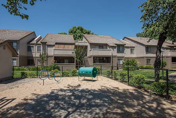 A dog park with a green barrel and two blue rings in front of apartment buildings at Zinfandel Village Apartments, California, 95670