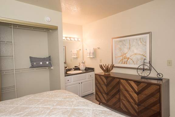 A bedroom with a bed, vanity, and a painting on the wall at Zinfandel Village Apartments, California, 95670