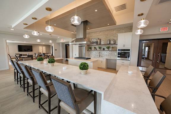 A long marble countertop with chairs and a kitchen in the background.