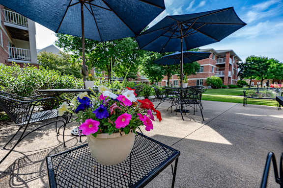 A flower pot with a mix of pink, red, and blue flowers sits on a table under a blue umbrella.