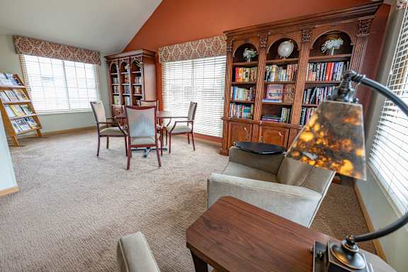 A living room with a brown carpet and a wooden bookcase.