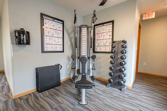 A gym room with a weight machine, a bench and a calendar on the wall.