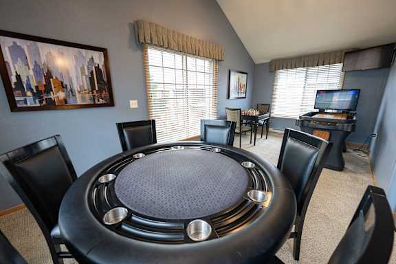A black table with a round top and silver legs is surrounded by black chairs in a room with a painting on the wall.